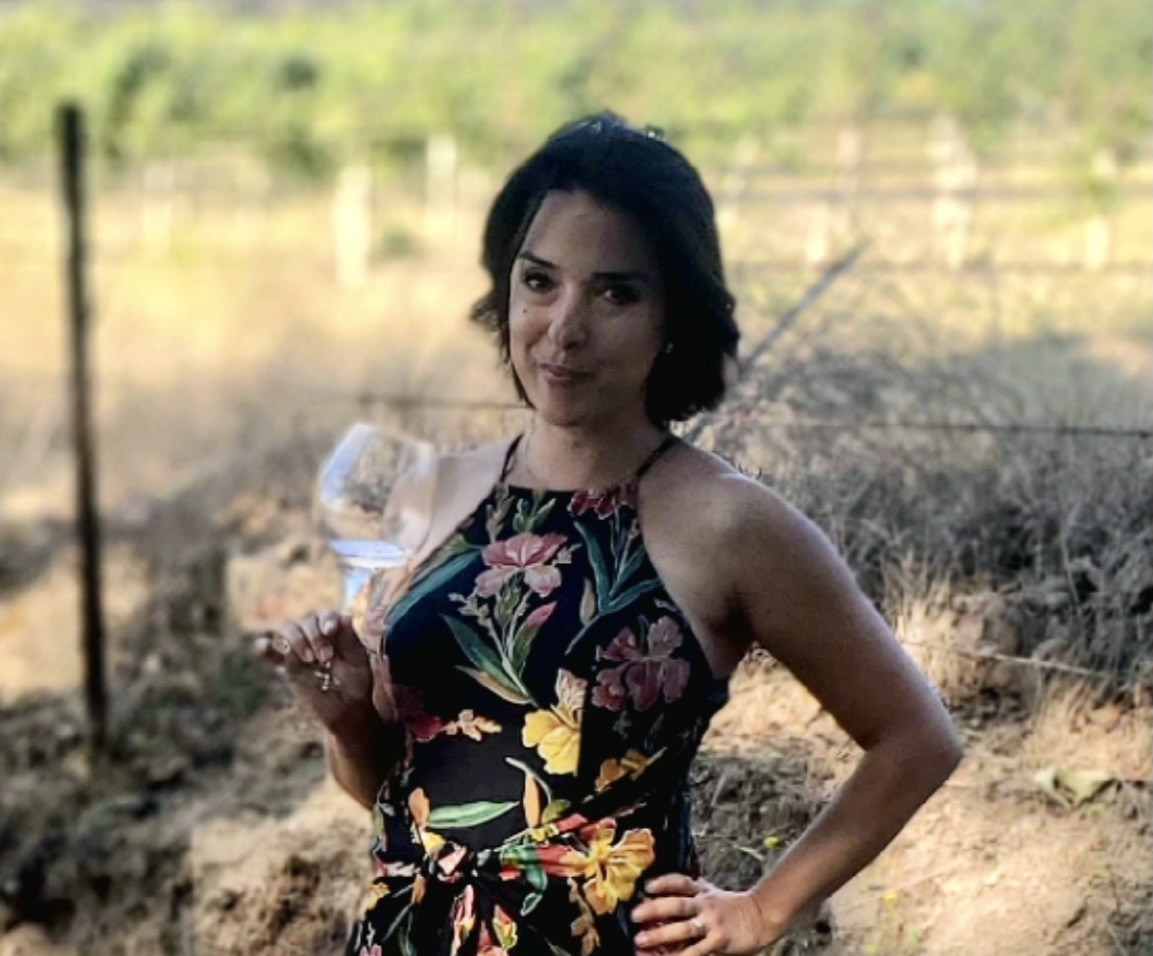 A picture of the writer of this piece, Anna Maria in a vineyard holding a wine glass